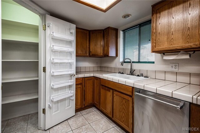 kitchen featuring light tile patterned floors, stainless steel dishwasher, a sink, and tile counters