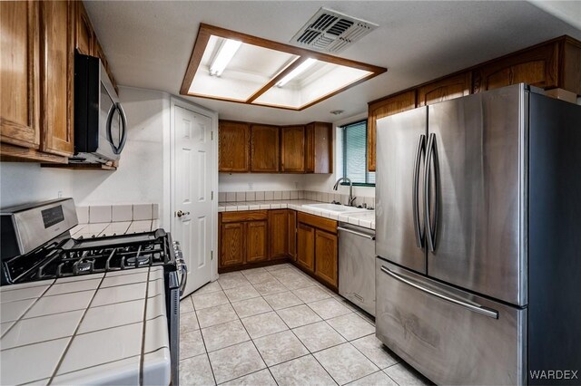 kitchen featuring visible vents, tile countertops, brown cabinets, stainless steel appliances, and a sink