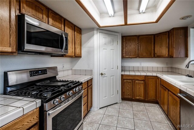 kitchen featuring stainless steel appliances, brown cabinets, a sink, and tile countertops