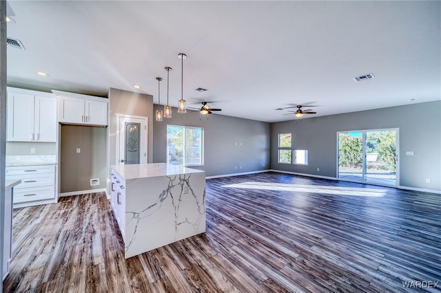 kitchen featuring decorative light fixtures, visible vents, open floor plan, white cabinetry, and a kitchen island