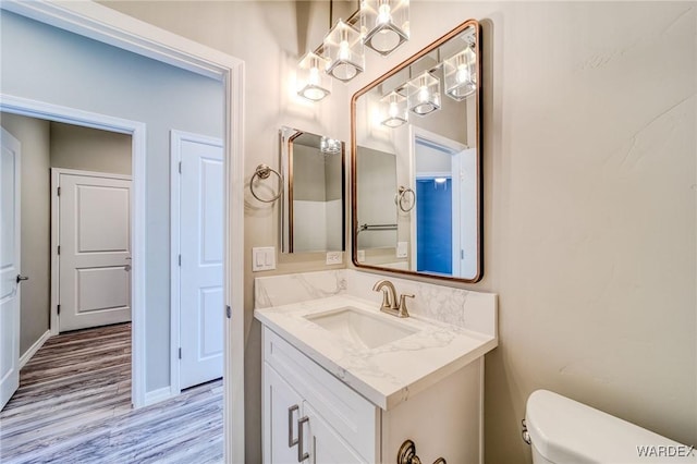 half bathroom featuring toilet, baseboards, wood finished floors, and vanity