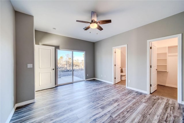 unfurnished bedroom with a walk in closet, access to exterior, baseboards, and light wood finished floors