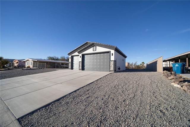 view of property exterior featuring stucco siding, concrete driveway, an attached garage, stone siding, and an outdoor structure