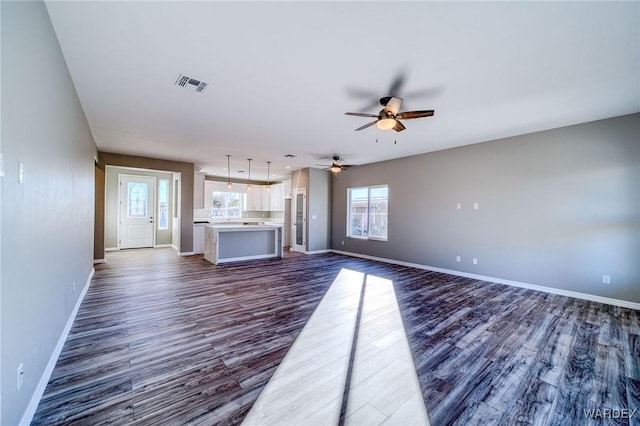 unfurnished living room featuring a ceiling fan, visible vents, dark wood finished floors, and baseboards