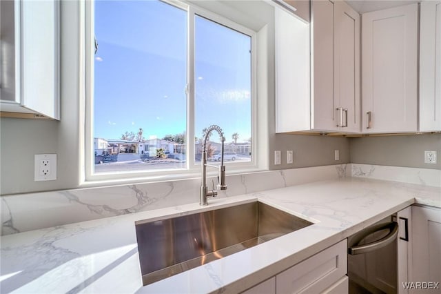 kitchen featuring white cabinets, a sink, dishwasher, and light stone countertops