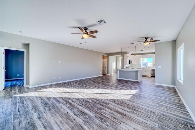 unfurnished living room featuring a ceiling fan, visible vents, baseboards, and wood finished floors