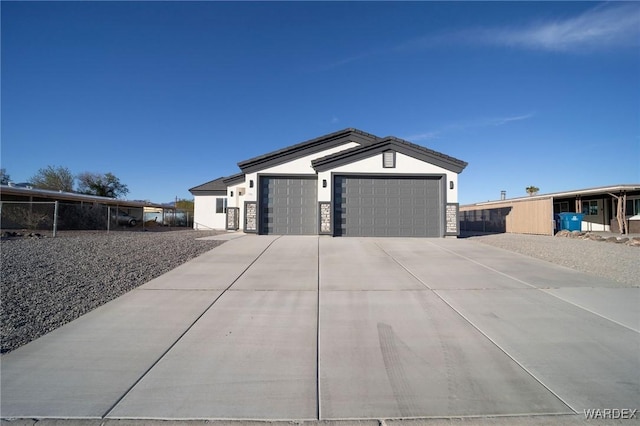 view of front facade with stone siding, driveway, an attached garage, and stucco siding