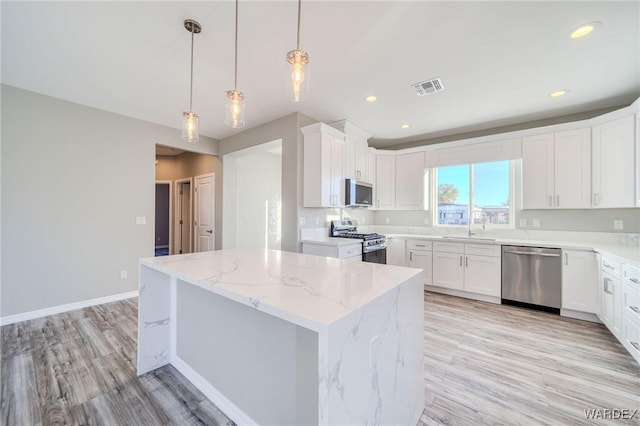 kitchen featuring visible vents, light stone counters, a center island, stainless steel appliances, and white cabinetry