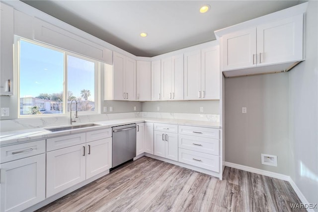 kitchen featuring stainless steel dishwasher, white cabinetry, a sink, light stone countertops, and light wood-type flooring