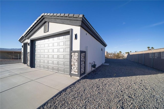 view of side of property with a garage, an outdoor structure, fence, and stucco siding