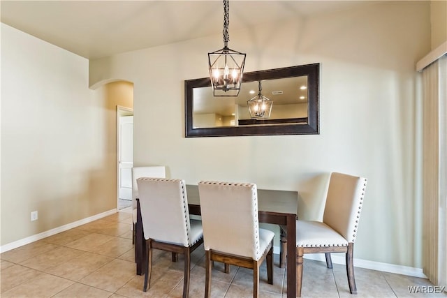 tiled dining space featuring baseboards, arched walkways, and a chandelier