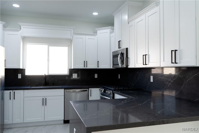 kitchen with appliances with stainless steel finishes, white cabinets, a sink, dark stone counters, and a peninsula