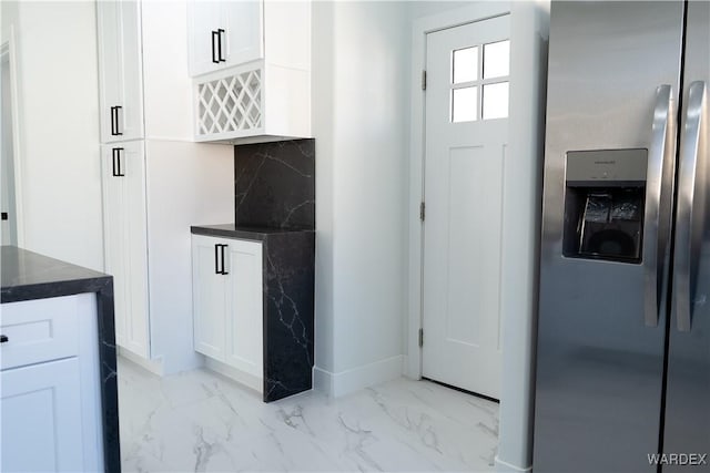 kitchen with marble finish floor, dark countertops, stainless steel fridge, and white cabinets