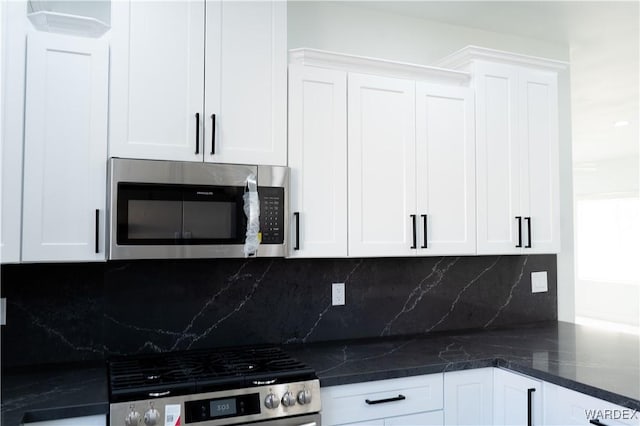 kitchen featuring appliances with stainless steel finishes, dark stone counters, white cabinets, and tasteful backsplash