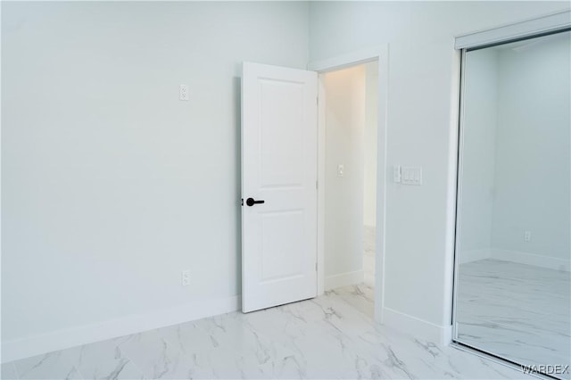 unfurnished bedroom with a closet, marble finish floor, and baseboards