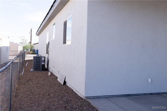 view of side of property with fence, central AC, and stucco siding