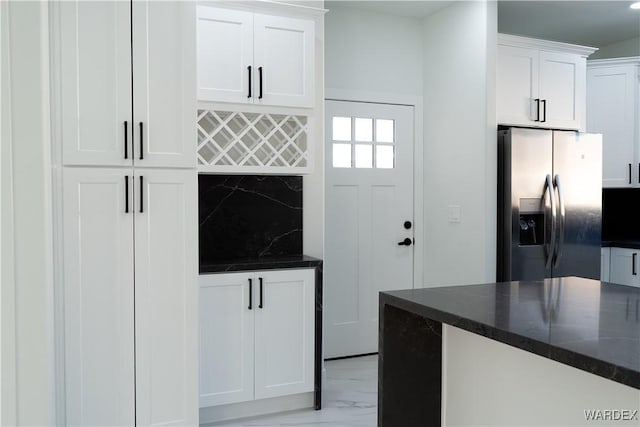 kitchen with dark stone counters, stainless steel fridge, white cabinetry, and decorative backsplash