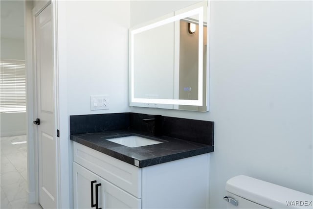 half bathroom featuring toilet, marble finish floor, and vanity