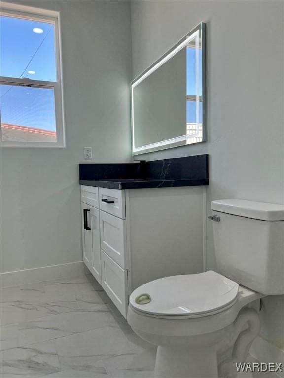 bathroom with toilet, marble finish floor, vanity, and baseboards