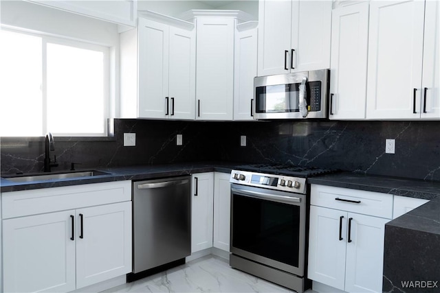 kitchen with a sink, white cabinets, marble finish floor, appliances with stainless steel finishes, and tasteful backsplash