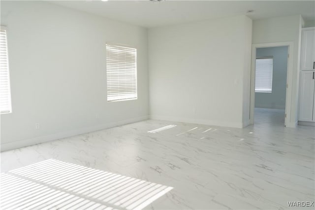 unfurnished room featuring a healthy amount of sunlight, marble finish floor, and baseboards