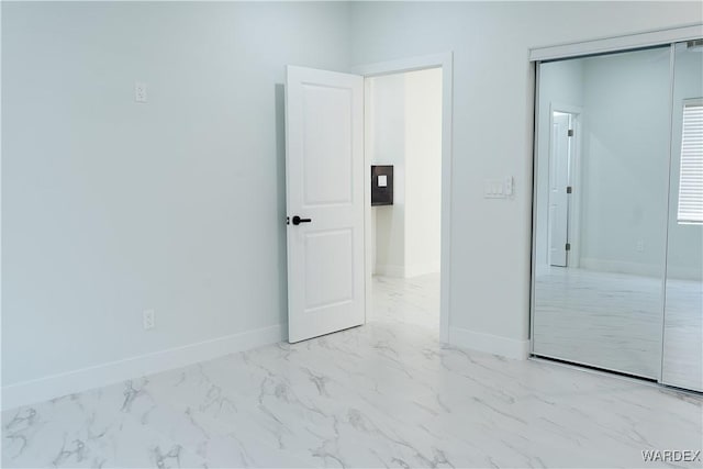 unfurnished bedroom with marble finish floor, a closet, and baseboards