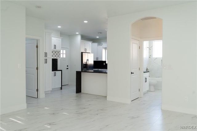 kitchen featuring arched walkways, white cabinetry, marble finish floor, stainless steel refrigerator with ice dispenser, and dark countertops