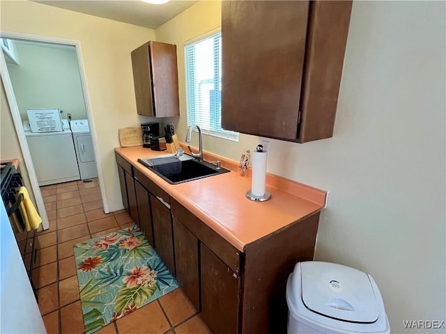 kitchen featuring washer and dryer, dark brown cabinets, a sink, and light countertops