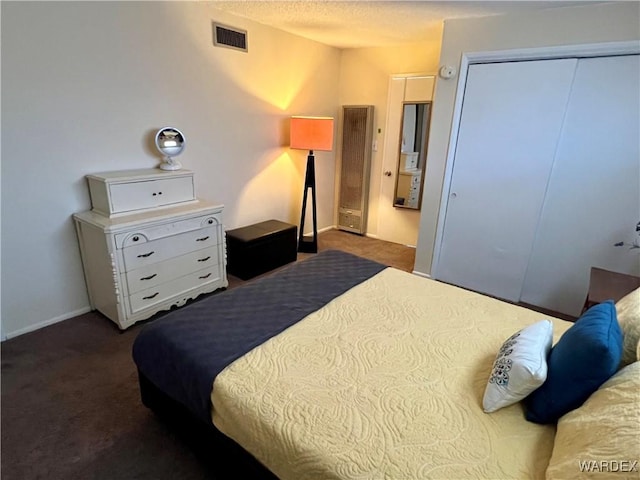 bedroom featuring a textured ceiling, dark colored carpet, a closet, and visible vents