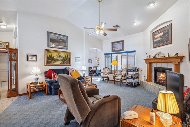 living area with ceiling fan, arched walkways, light colored carpet, visible vents, and a tiled fireplace