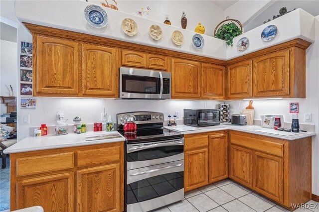 kitchen featuring appliances with stainless steel finishes, brown cabinetry, light countertops, and light tile patterned floors