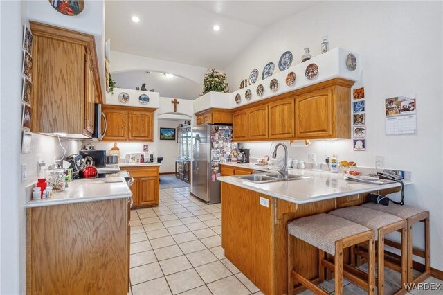 kitchen featuring a breakfast bar area, a peninsula, stainless steel appliances, light countertops, and a sink