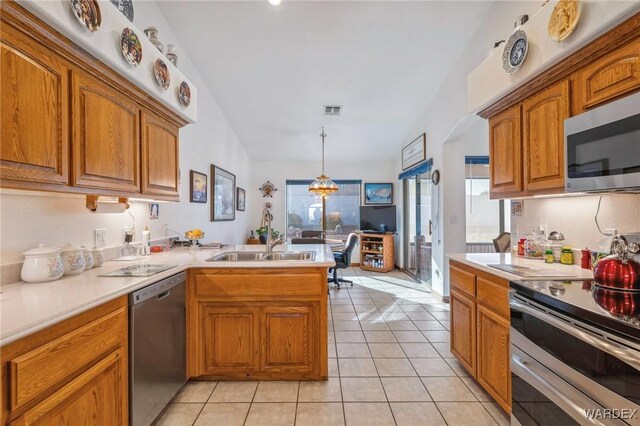 kitchen featuring a peninsula, light countertops, appliances with stainless steel finishes, brown cabinetry, and pendant lighting