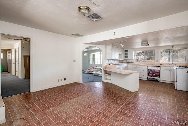 kitchen with arched walkways, light countertops, visible vents, white cabinets, and beverage cooler