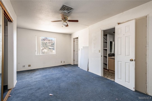 unfurnished bedroom featuring a textured ceiling, ceiling fan, dark carpet, and visible vents