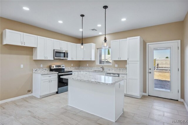 kitchen featuring white cabinets, a center island, light stone countertops, stainless steel appliances, and a sink