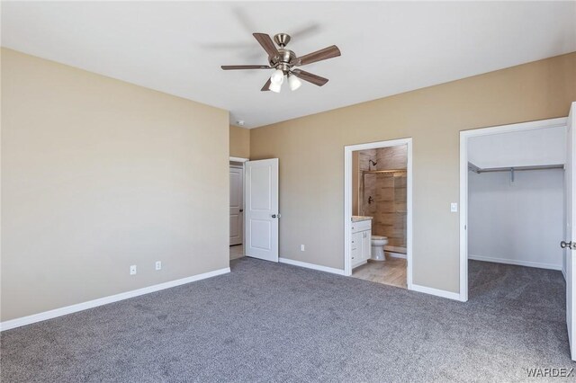 unfurnished bedroom with a walk in closet, light colored carpet, ensuite bath, and baseboards