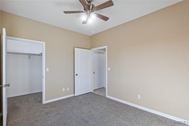 unfurnished bedroom featuring carpet floors, a ceiling fan, baseboards, a closet, and a walk in closet