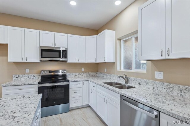 kitchen with stainless steel appliances, light stone counters, a sink, and white cabinets