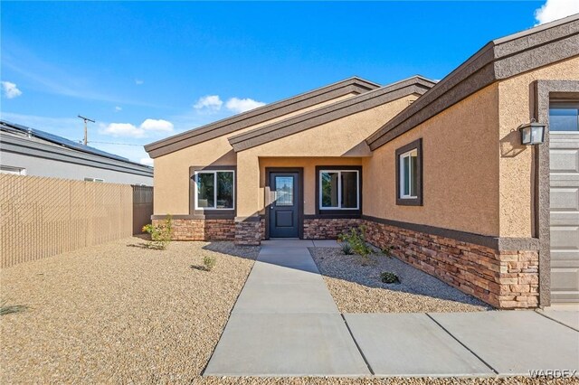 doorway to property featuring stone siding, fence, and stucco siding