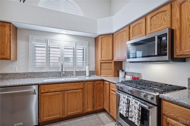 kitchen with stainless steel appliances, brown cabinets, a sink, and light tile patterned floors