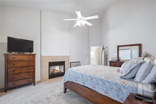 bedroom featuring light carpet, ceiling fan, a towering ceiling, and a tile fireplace