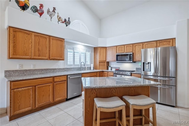 kitchen with a center island, brown cabinets, a breakfast bar area, stainless steel appliances, and high vaulted ceiling