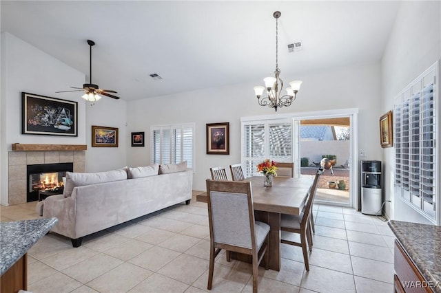 dining space featuring ceiling fan with notable chandelier, a tile fireplace, visible vents, and light tile patterned floors