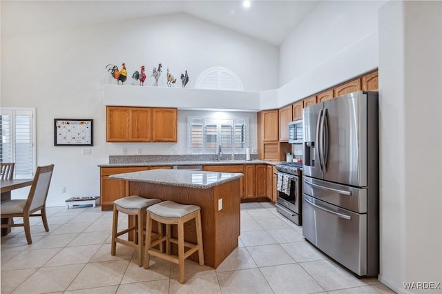 kitchen with a center island, brown cabinets, stainless steel appliances, light tile patterned flooring, and a kitchen breakfast bar