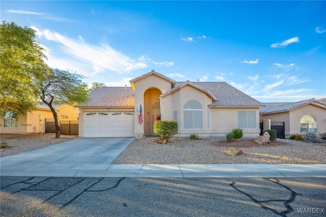 mediterranean / spanish home featuring concrete driveway, a tile roof, an attached garage, fence, and stucco siding