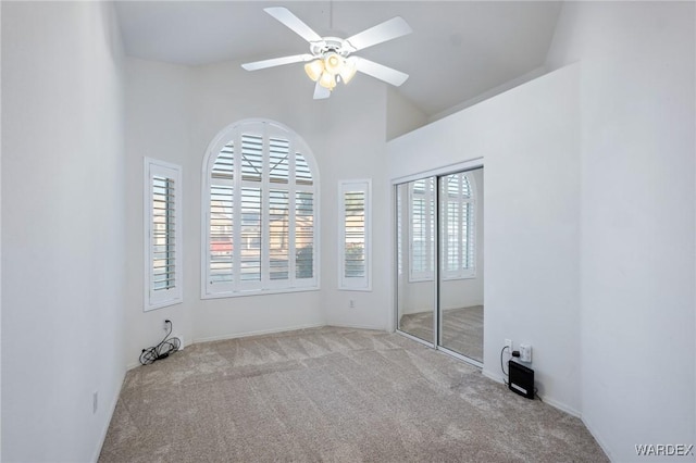 spare room with ceiling fan, high vaulted ceiling, and light colored carpet