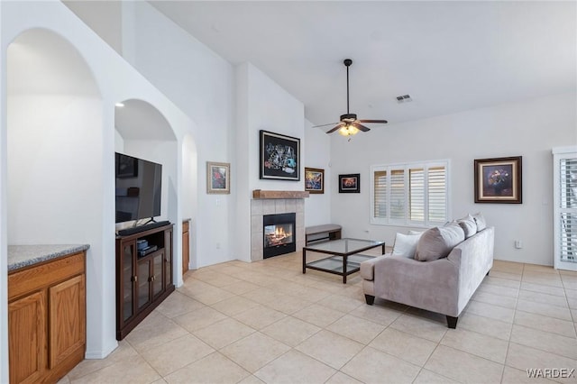 living area with a fireplace, light tile patterned floors, visible vents, ceiling fan, and high vaulted ceiling