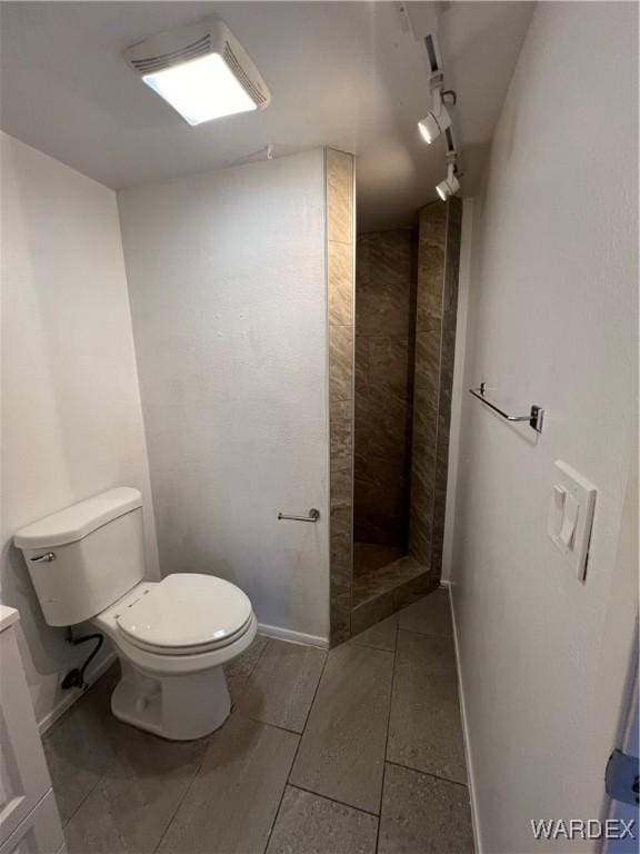 full bath with rail lighting, a tile shower, toilet, and baseboards