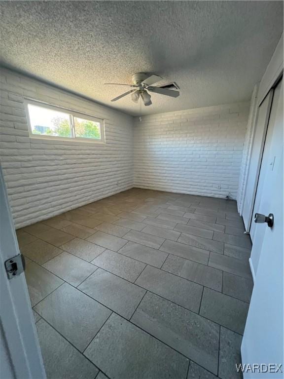 unfurnished room with ceiling fan, a textured ceiling, and brick wall